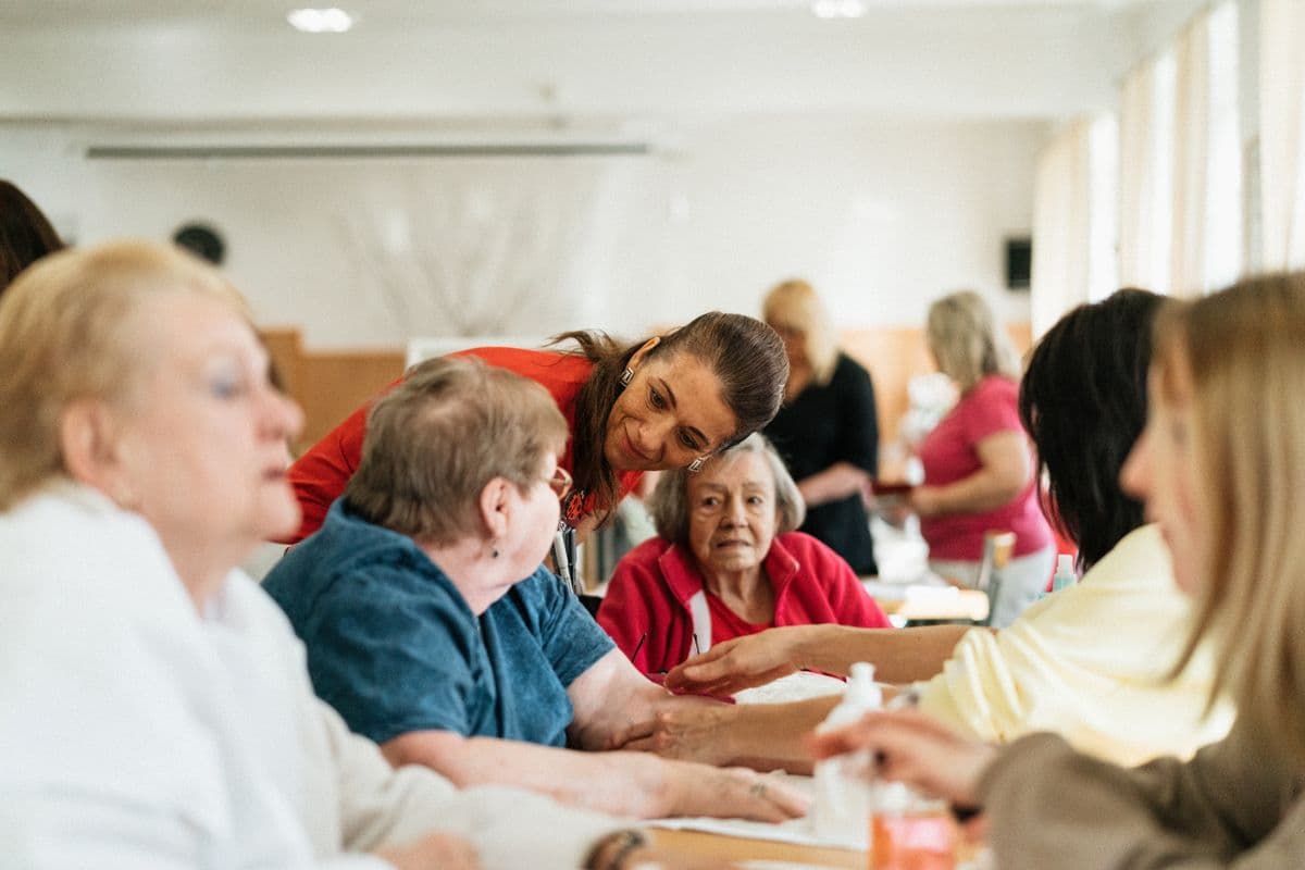A caregiver leaning in with residents at a supported-living table